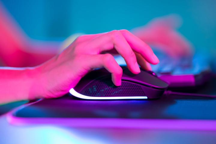 A hand using a mouse on a mouse pad, with a colorful, neon-lit background.