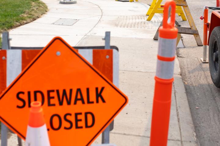 A construction scene in Saskatoon including orange pylons and a "sidewalk closed" sign