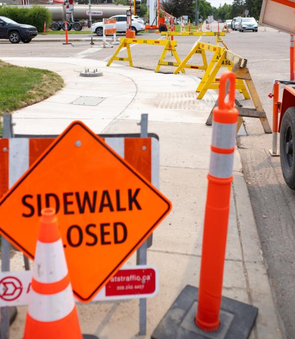 A construction scene in Saskatoon including orange pylons and a "sidewalk closed" sign