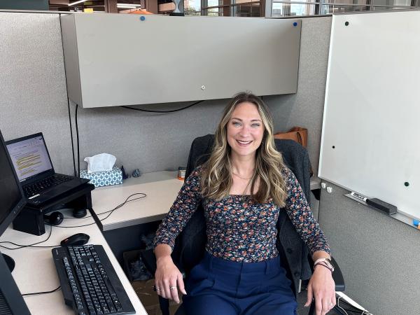 Photo of a woman sitting at a desk in an office environment, posing for a casual yet professional photo.