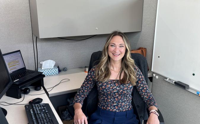Photo of a woman sitting at a desk in an office environment, posing for a casual yet professional photo.